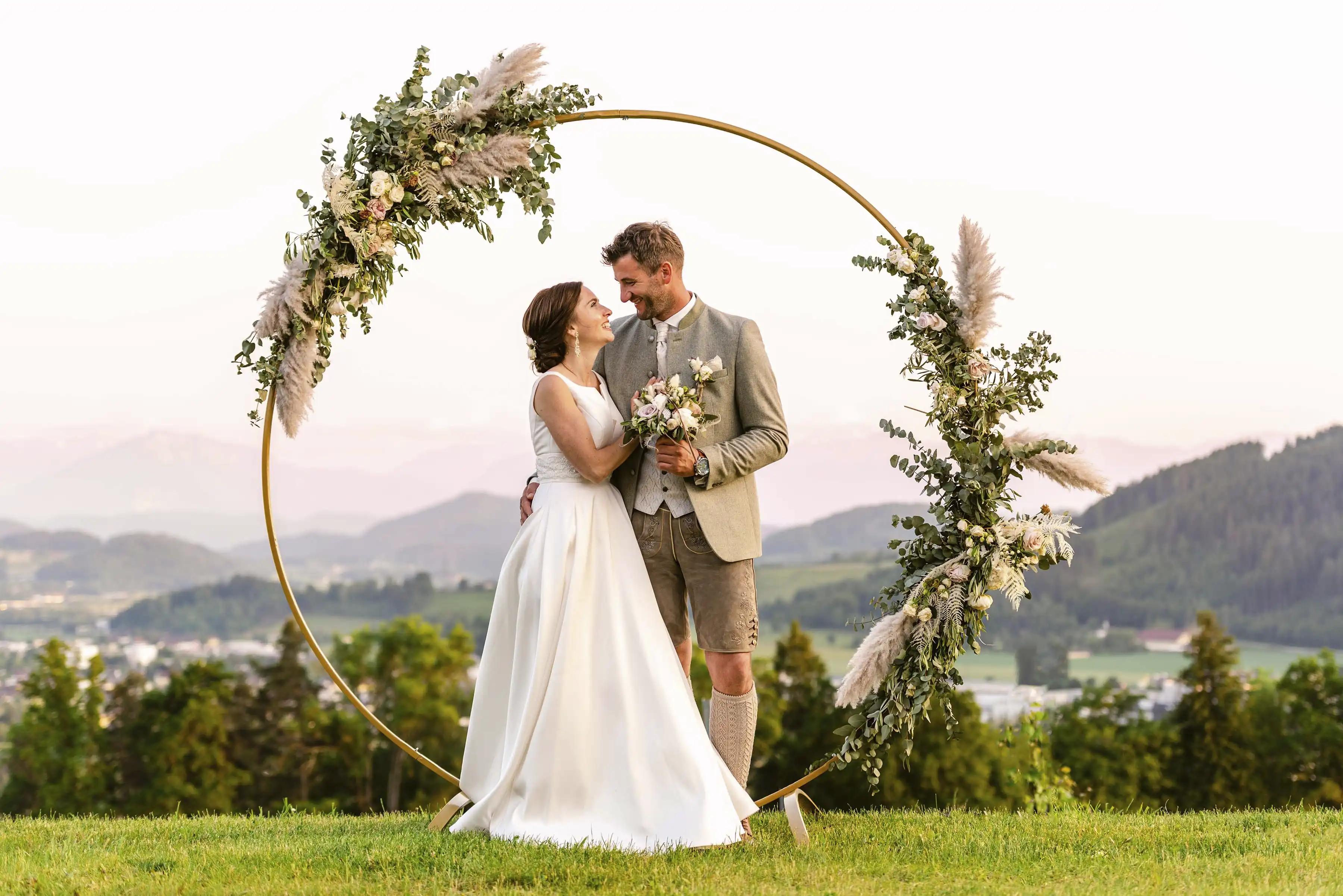 Hochzeitspaar auf einer Anhöhe mit einem dekorierten Holzring(Wedding Hoop) im Hintergrund