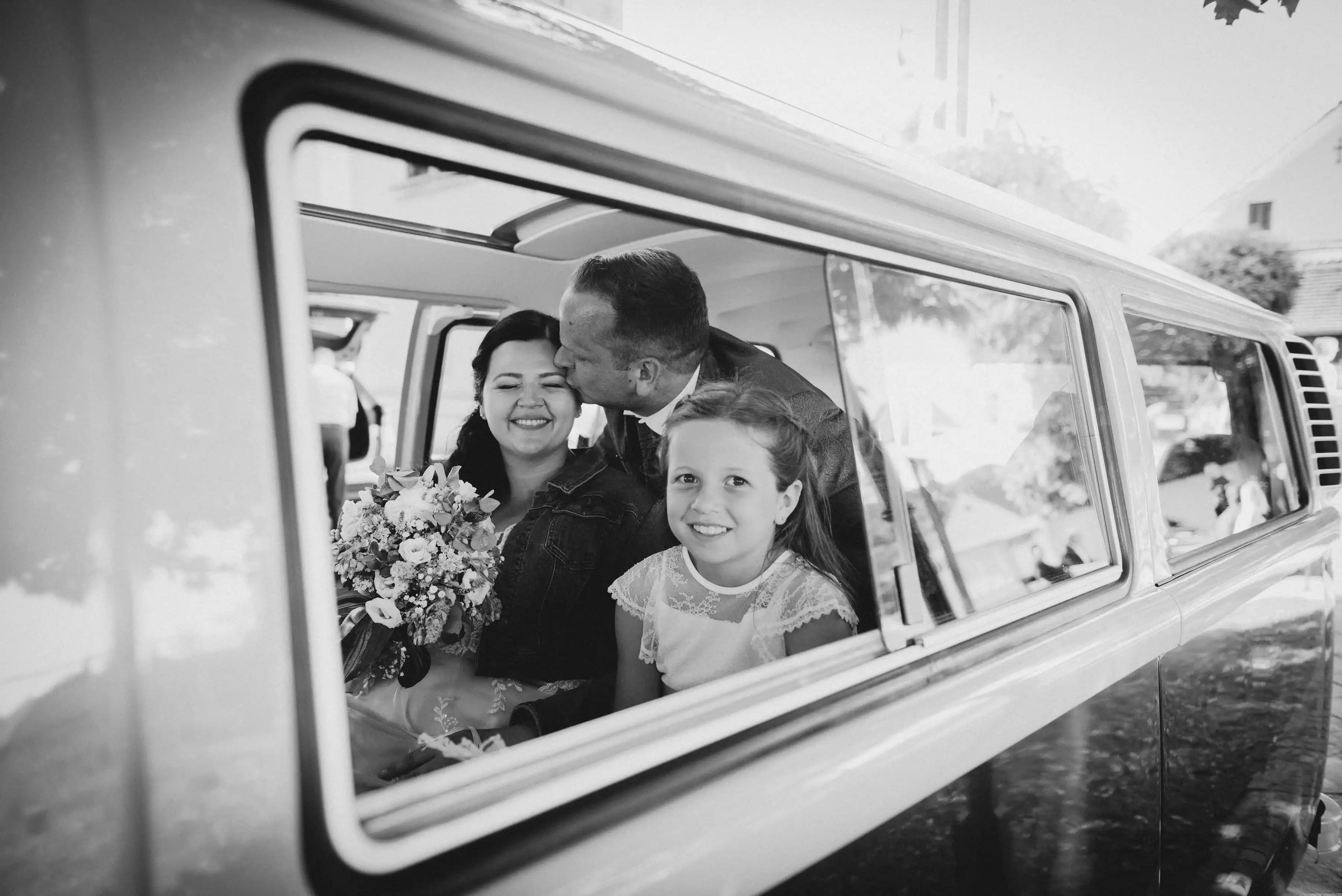 Bräutigam küsst Braut in einem VW Bus(Bulli) auf die Wange.