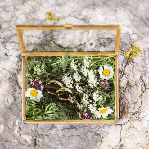 Eine kleine Glastruhe mit Wiesenblumen und zwei Eheringen darin.